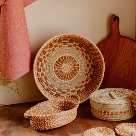 Small pine needle basket with handles in front of a larger green and brown basket and next to a green tortilla basket.