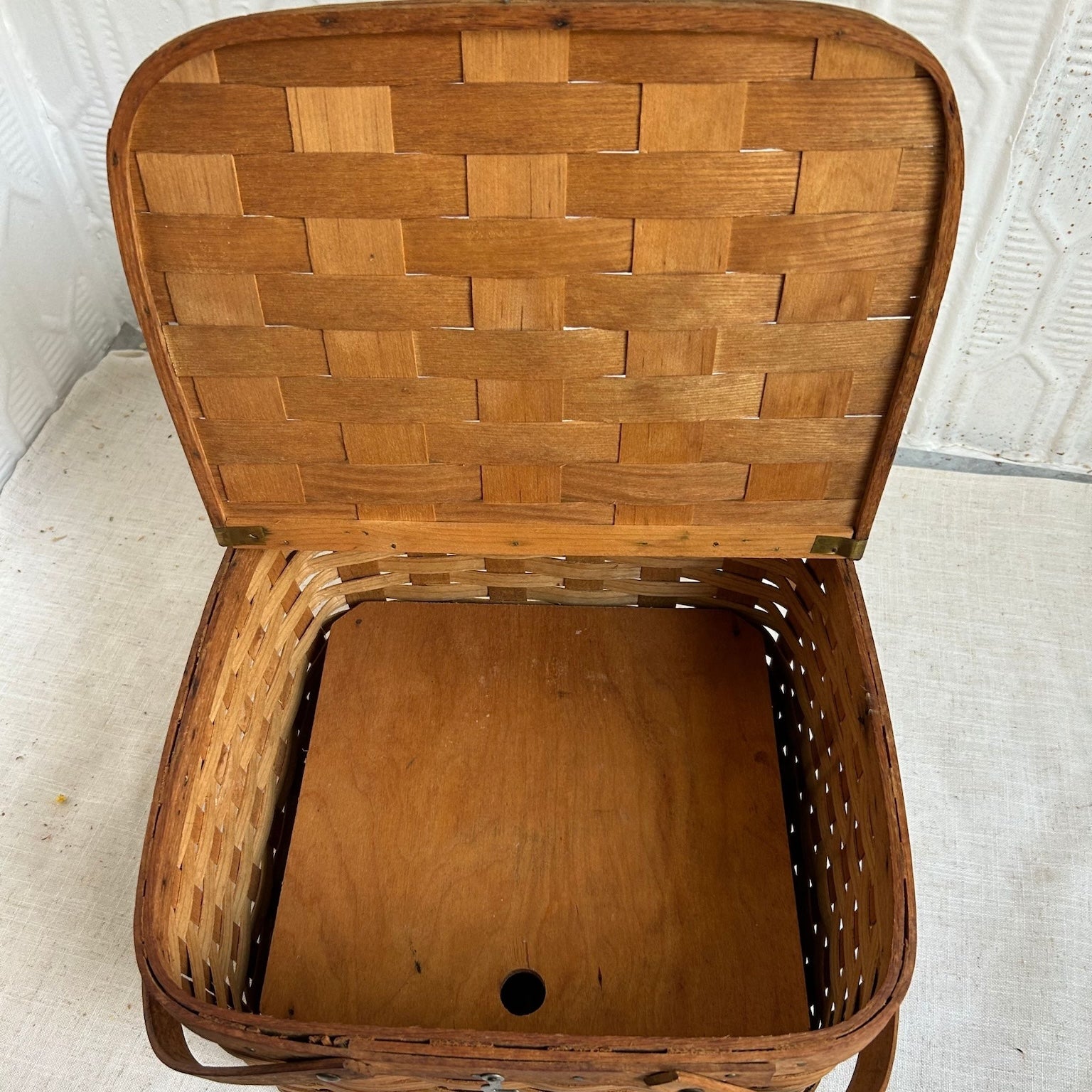 A vintage woven wooden picnic basket with its lid propped open, showing a natural brown wood grain finish and interlaced basket weave pattern.
