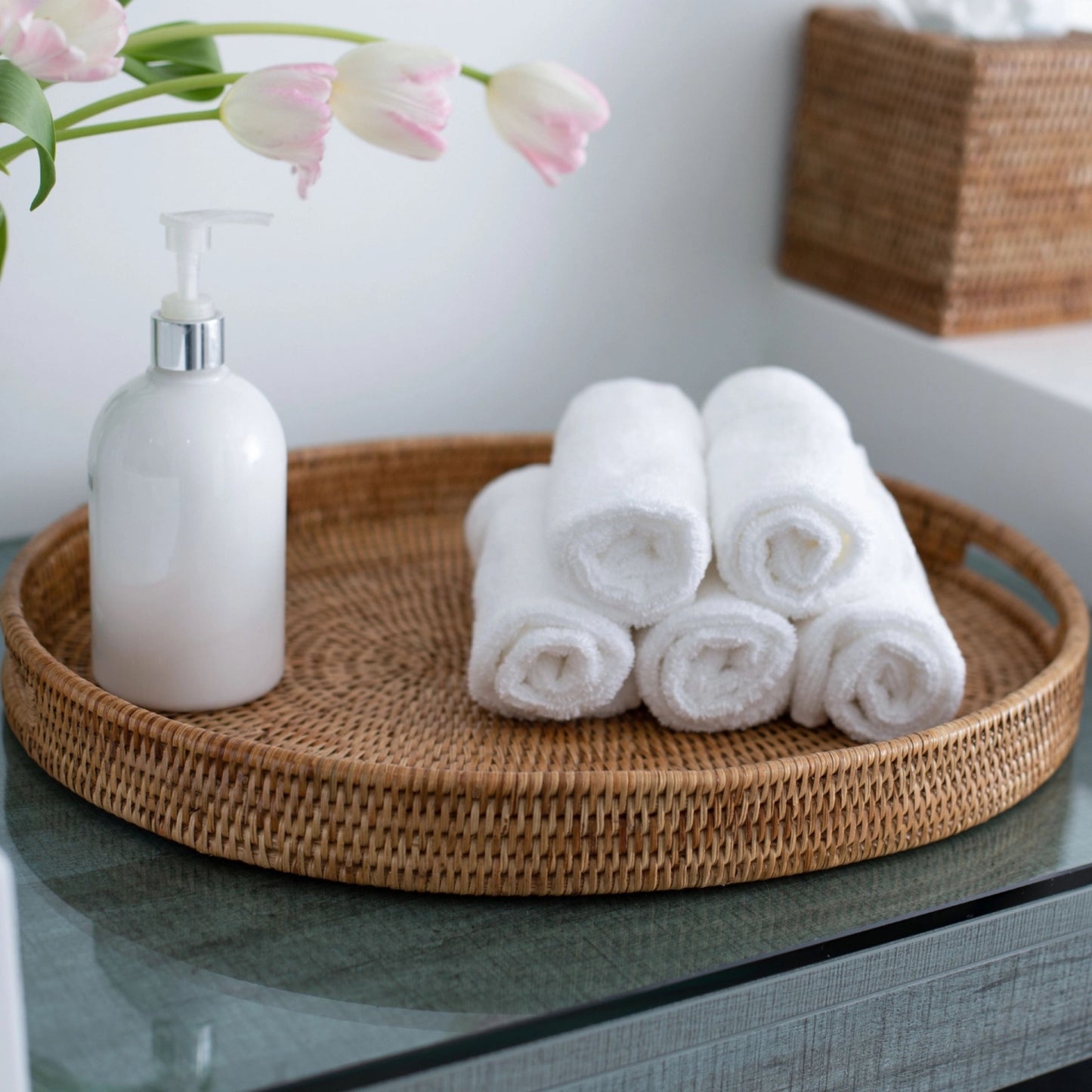 White towels and a bottle on a woven tray with pink flowers in the background