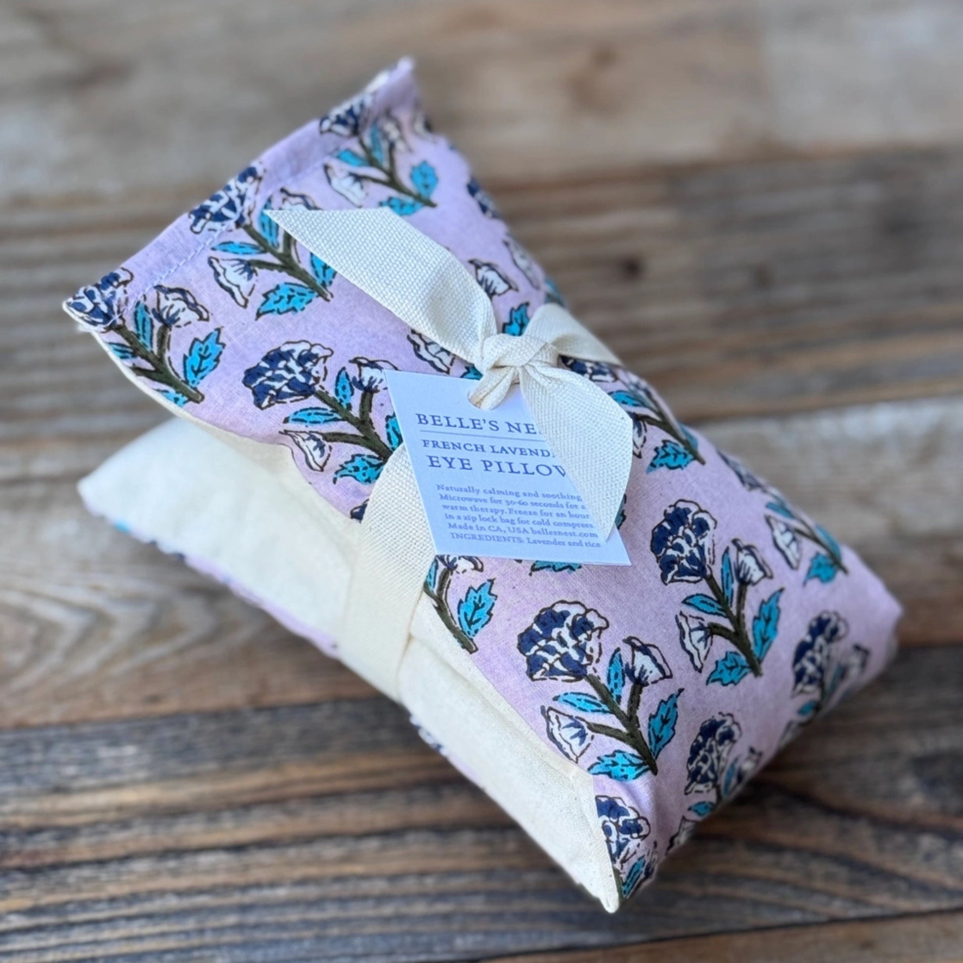 Floral-patterned eye pillow with a tag on a wooden surface