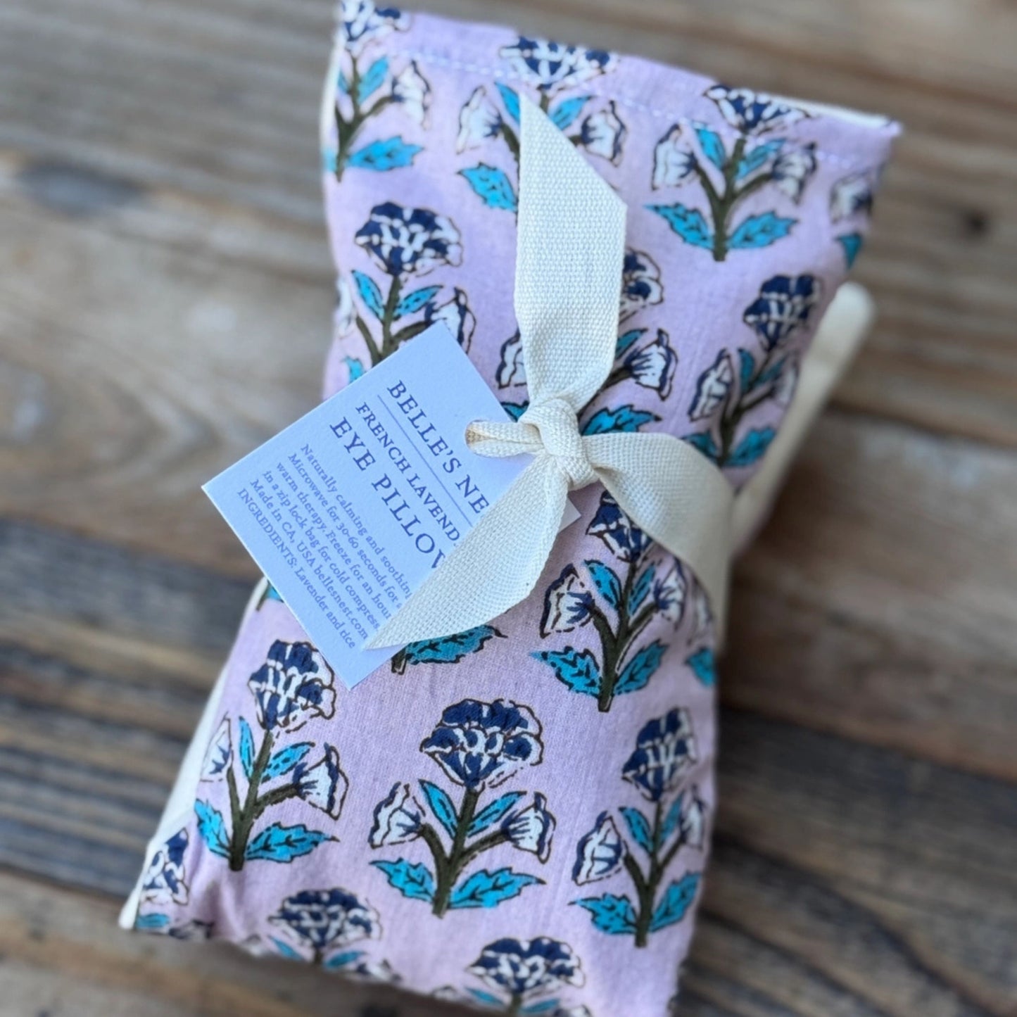 Floral-patterned eye pillow with a tag on a wooden surface