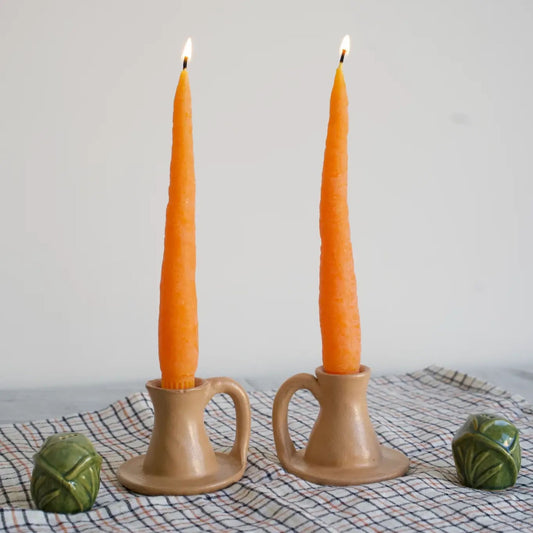 Two tall carrot-shaped candles in beige candle holders on a checkered tablecloth.