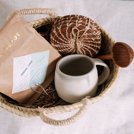 Woven basket with a mug, tea, a coffee scoop, and coasters on a light background
