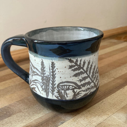 Ceramic mug with black handle and botanical design on a wooden surface