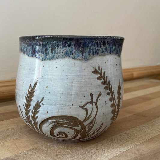 Ceramic mug with blue rim and brown floral patterns on a wooden surface