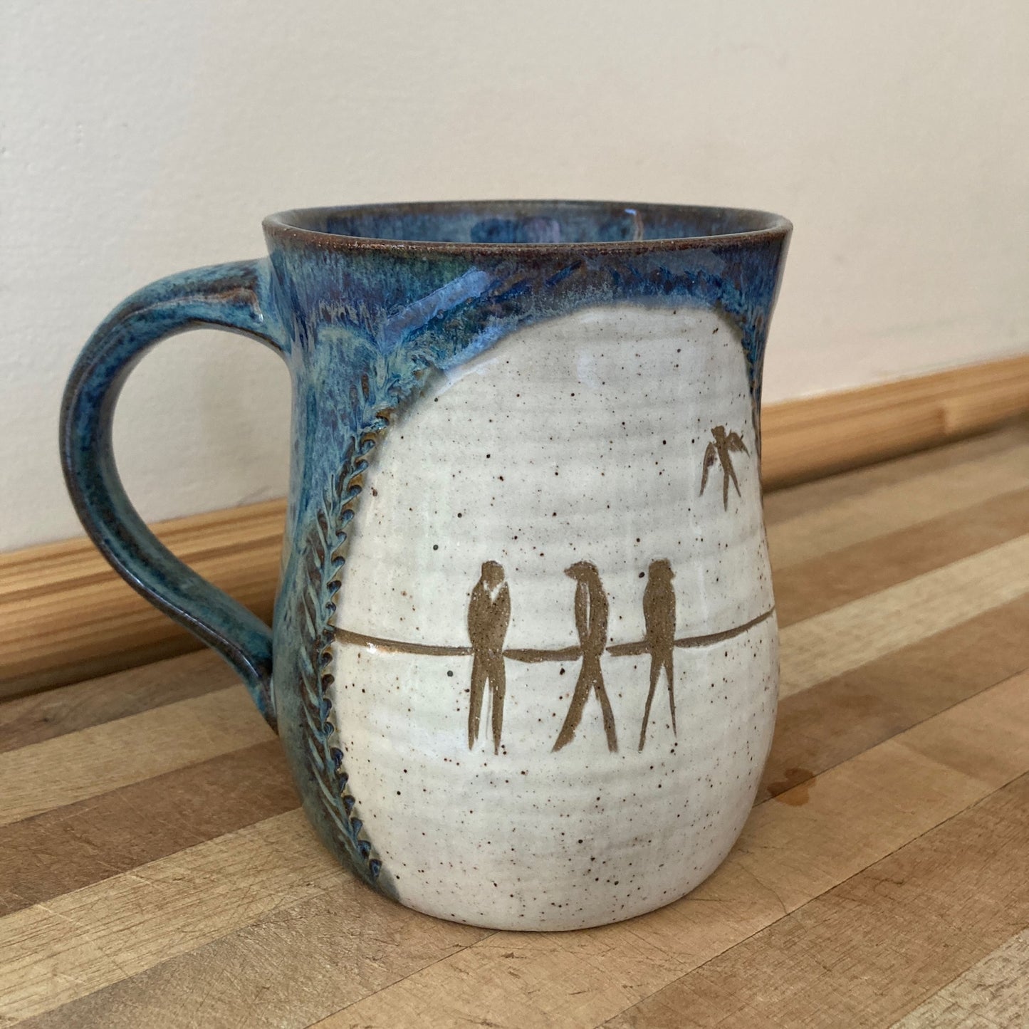 Ceramic mug with blue handle and brown birds on a wooden surface