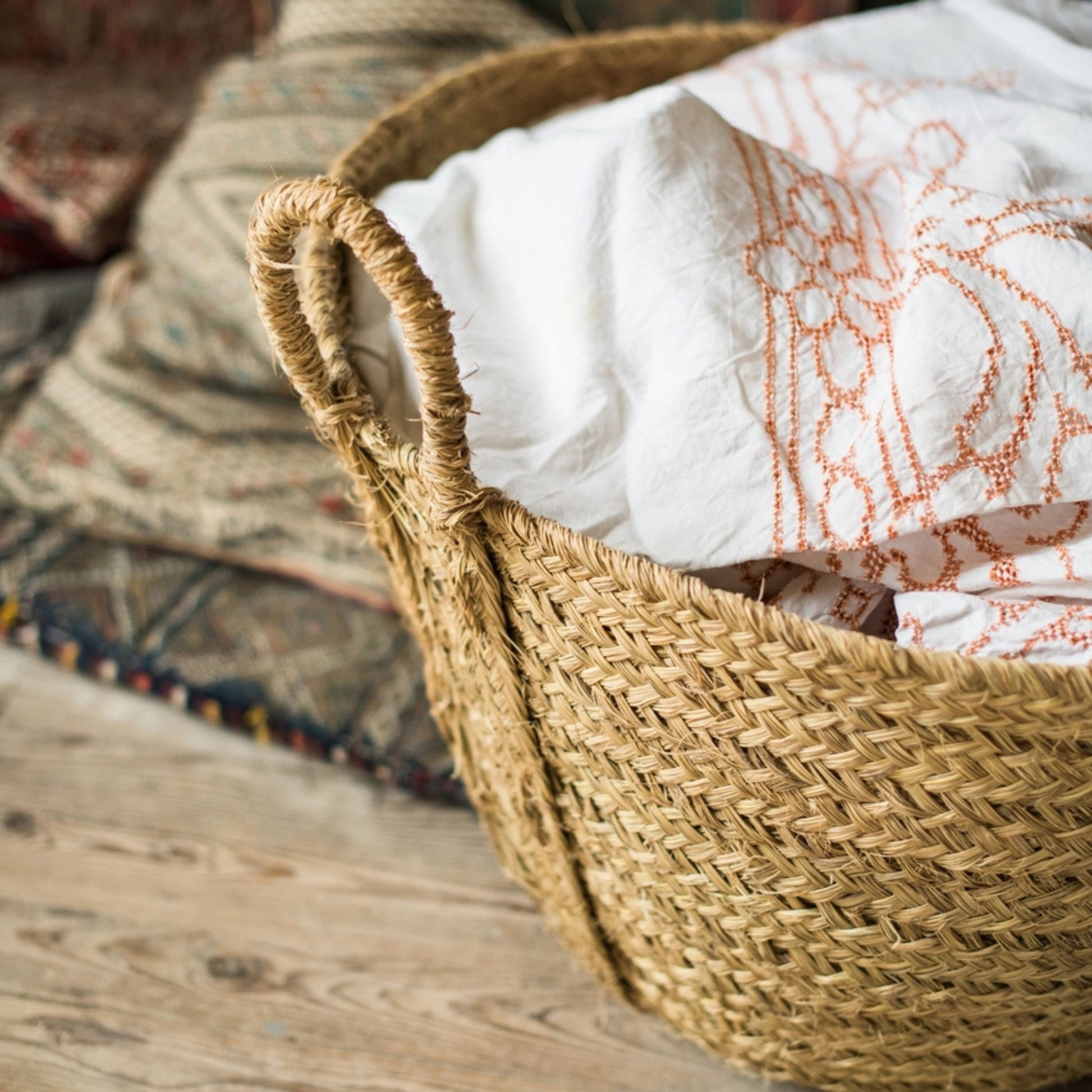 Woven basket with a white fabric with orange patterns on a wooden surface