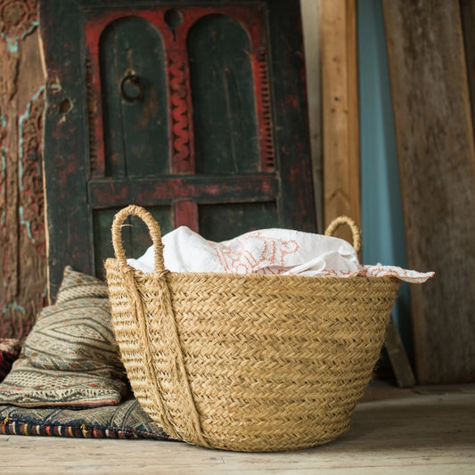 Woven basket with white fabric inside, placed on a wooden floor with a rustic background.