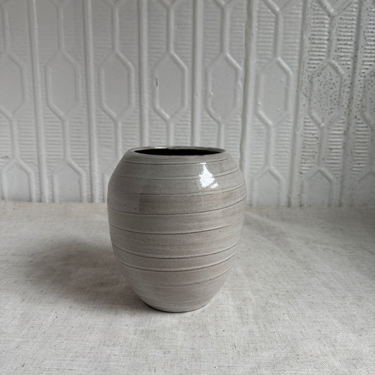Gray ceramic vase on a textured surface with a geometric patterned wall in the background