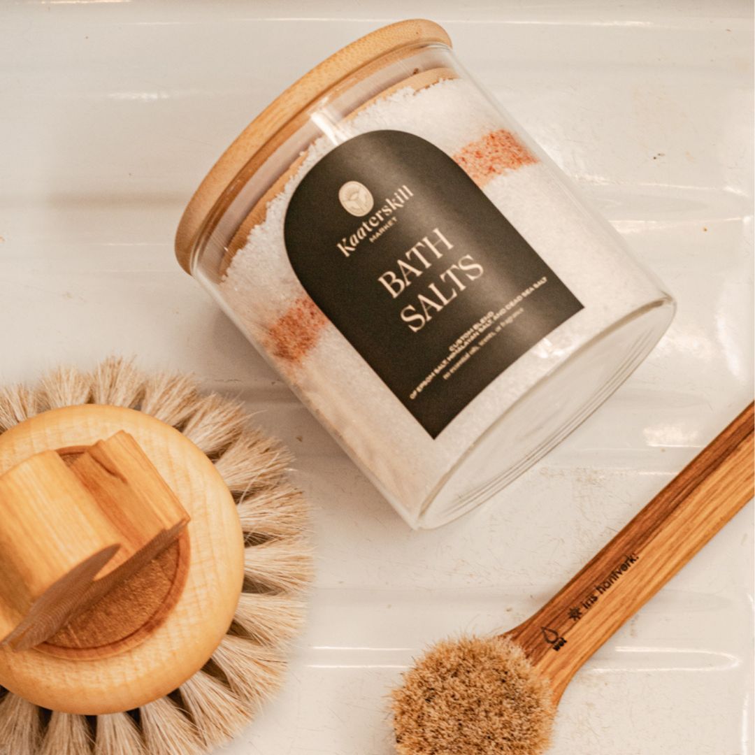 epsom salt and pink himalyan bath salt in a reusable glass jar with bamboo lid pictured with a bath brush and face cleansing brush