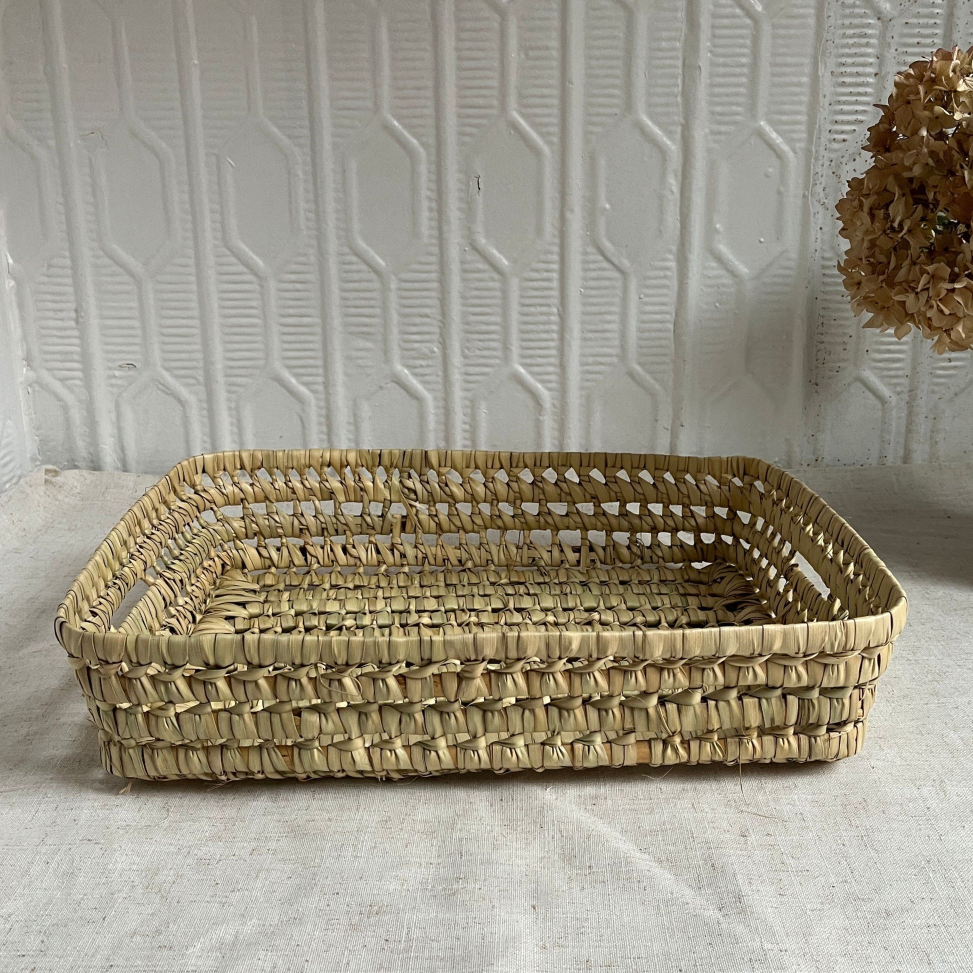 Woven rectangular basket on a textured surface with a white wall background
