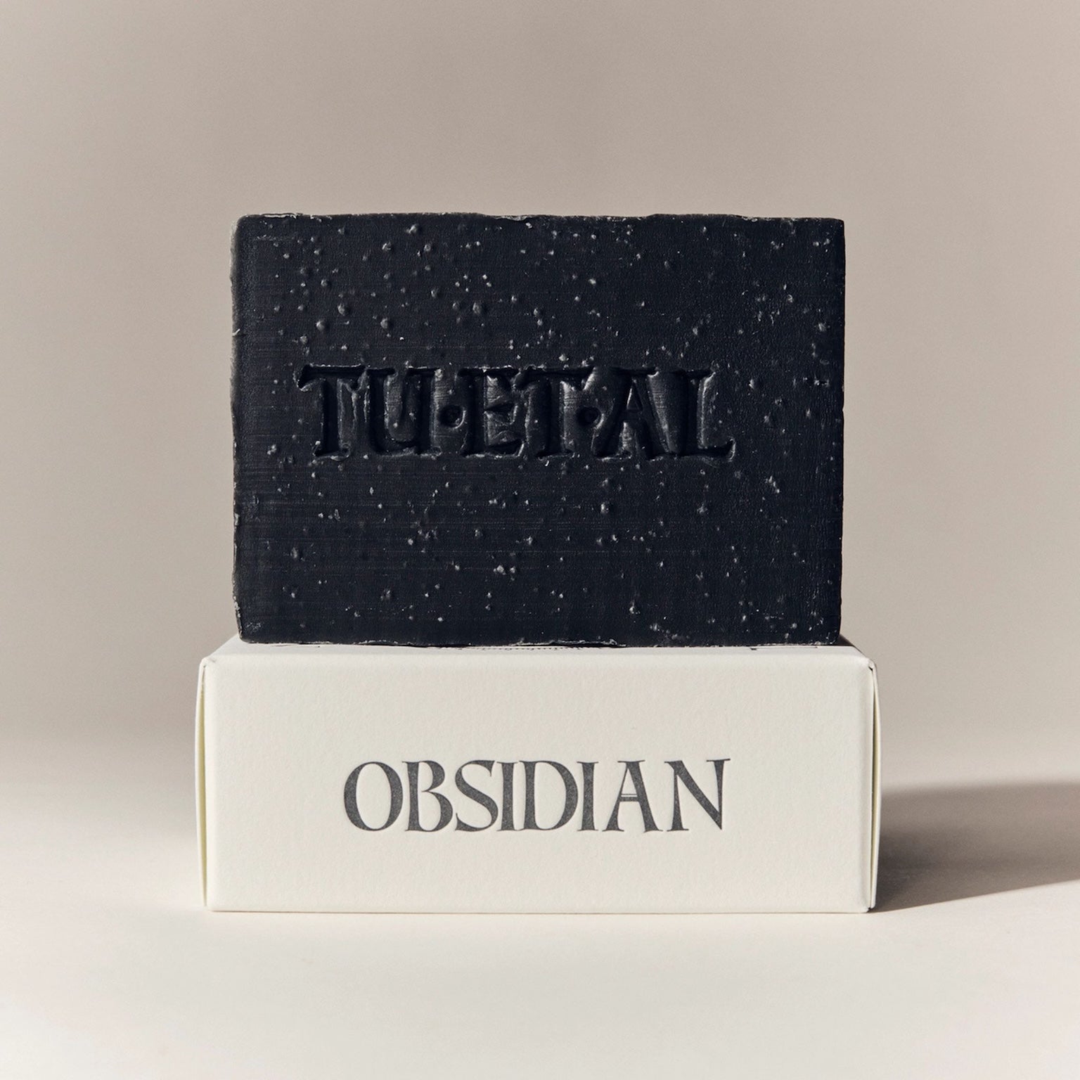 Black soap bar with 'TU.ET.AL' branding on a beige background