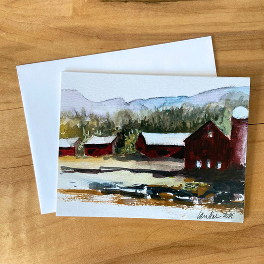 A blank greeting card depicting three barns surrounded by forest and mountains. This Hudson Valley artist, Laura Avello, creates this imagery by mixing watercolor and printmaking.