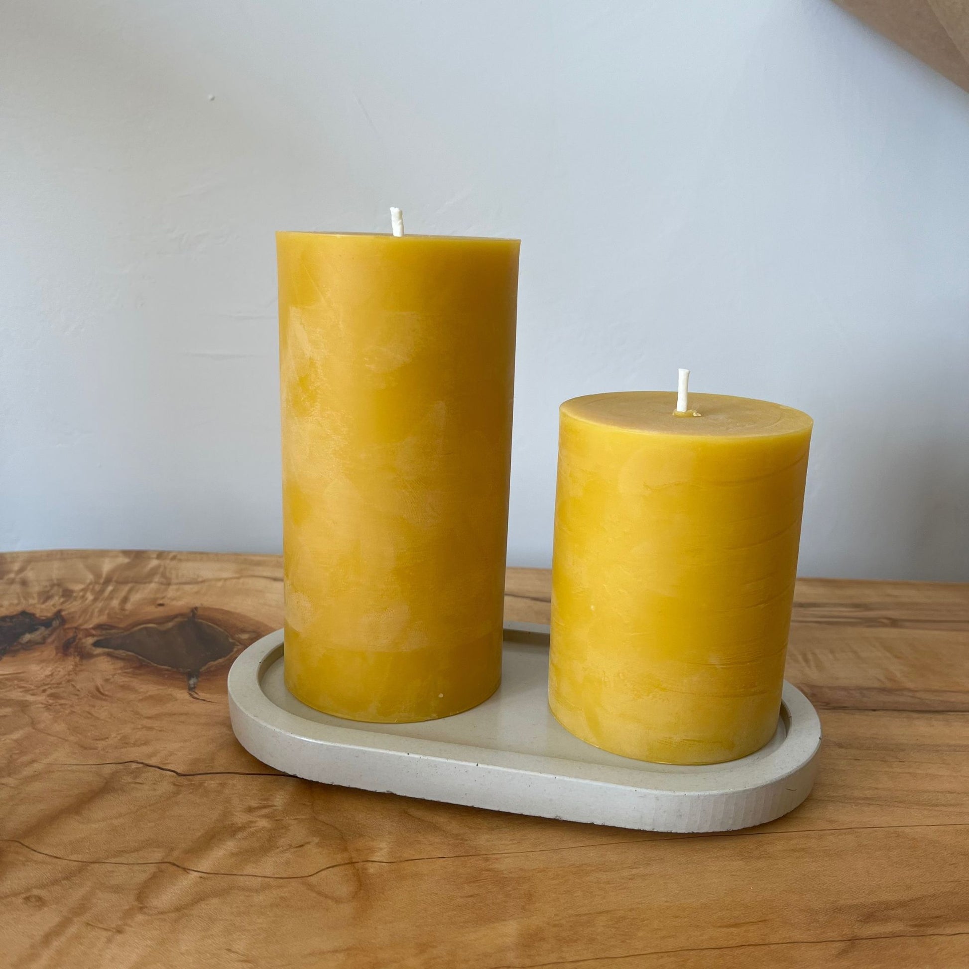 4 inch beeswax candle on a ceramic plate next to a bigger candle