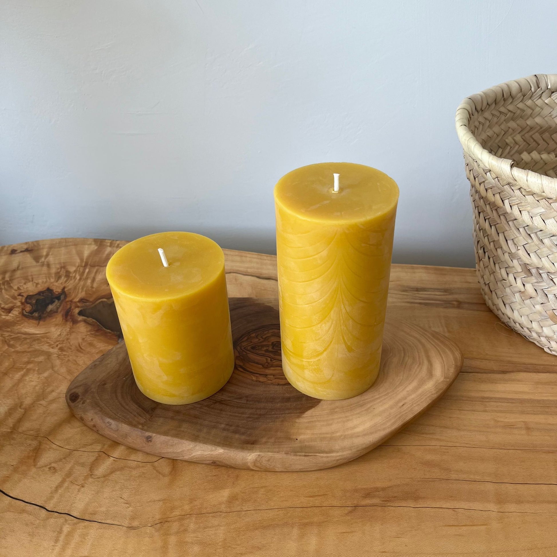 two beeswa candles in different sizes on a wooden plate