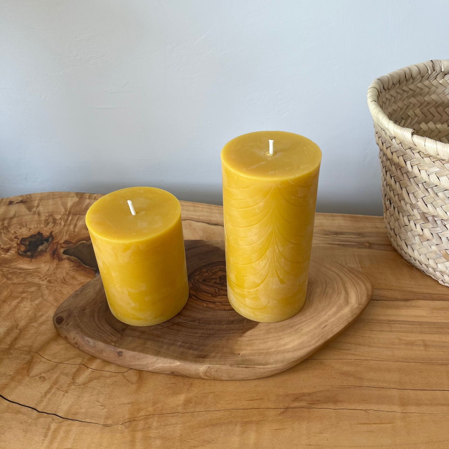 Two beeswax candles of different sizes on a wooden plate