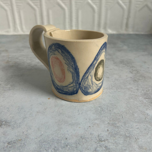 A white mug with blue circles and red and green smaller circles within each blue one.
