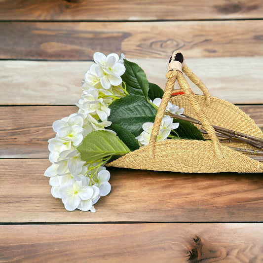 Wicker basket with white flowers and green leaves on a wooden surface