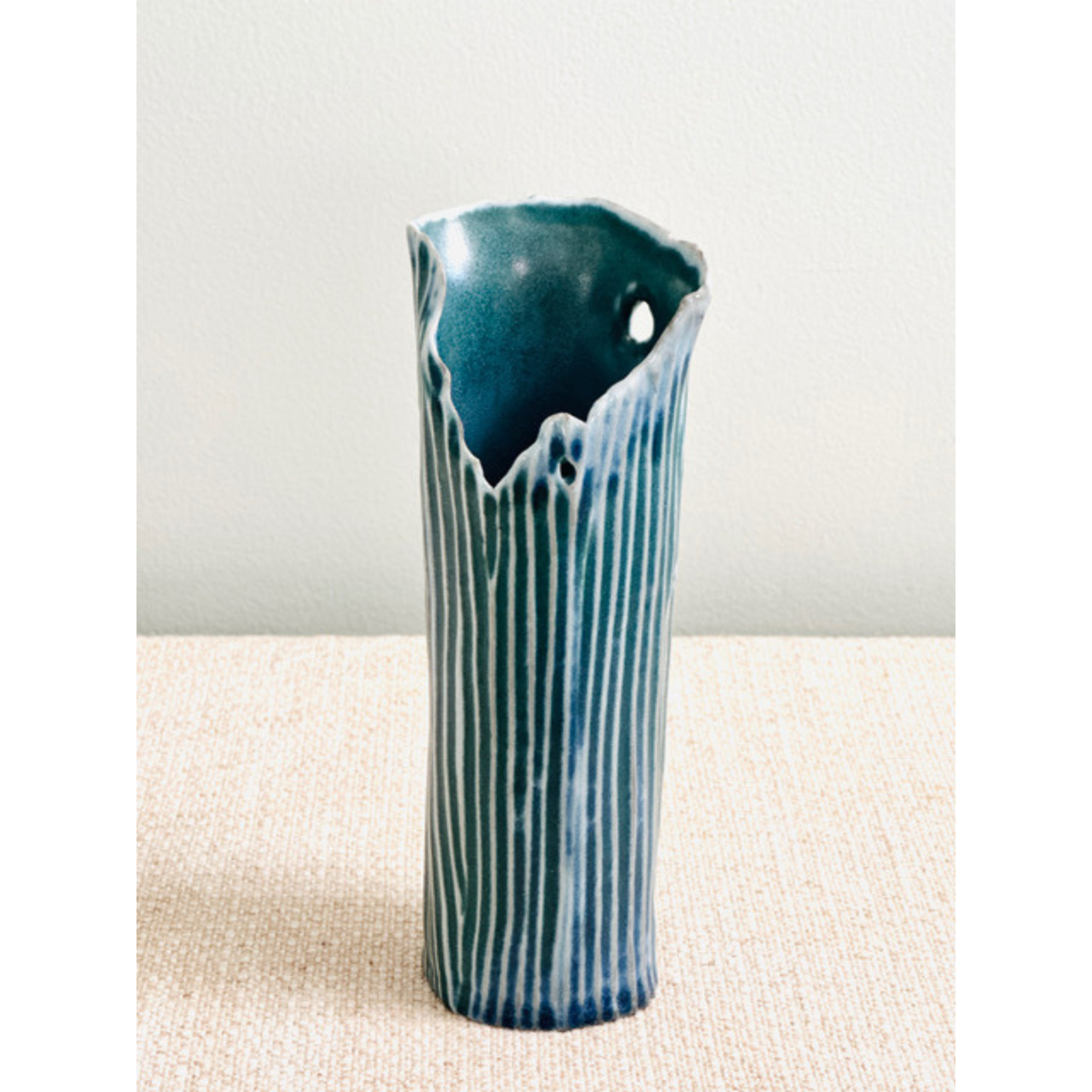 Blue ceramic vase with striped pattern on a beige surface