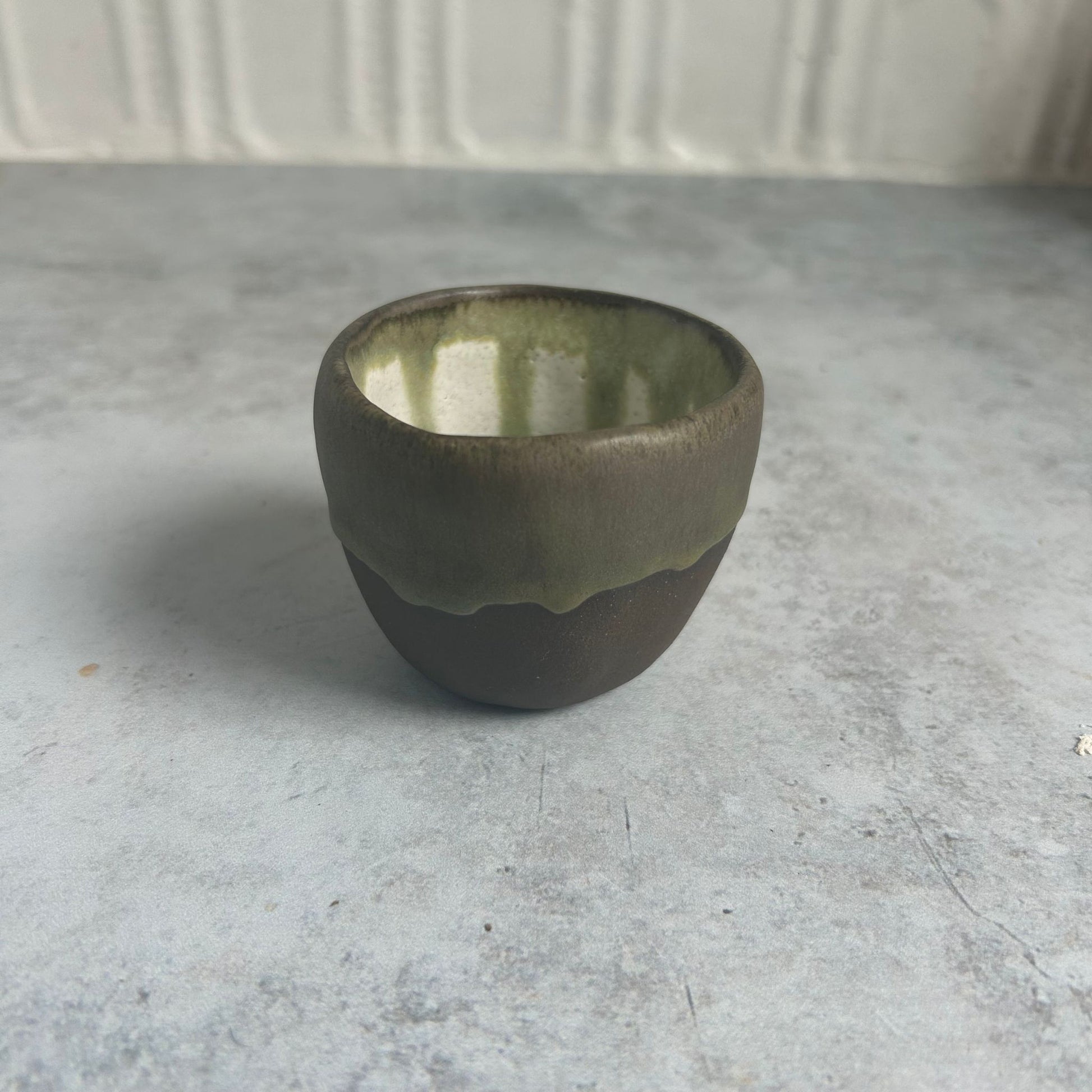 A small brown cup with a white and green drip inside. 