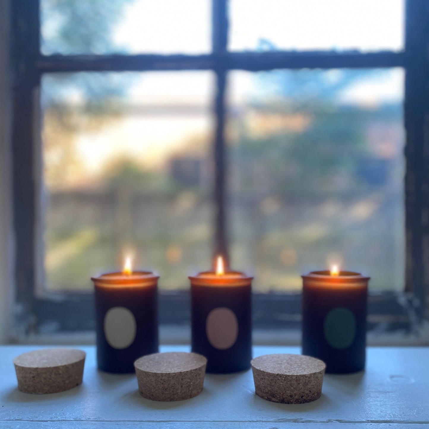 three essential oil candles lightened up in front of a window