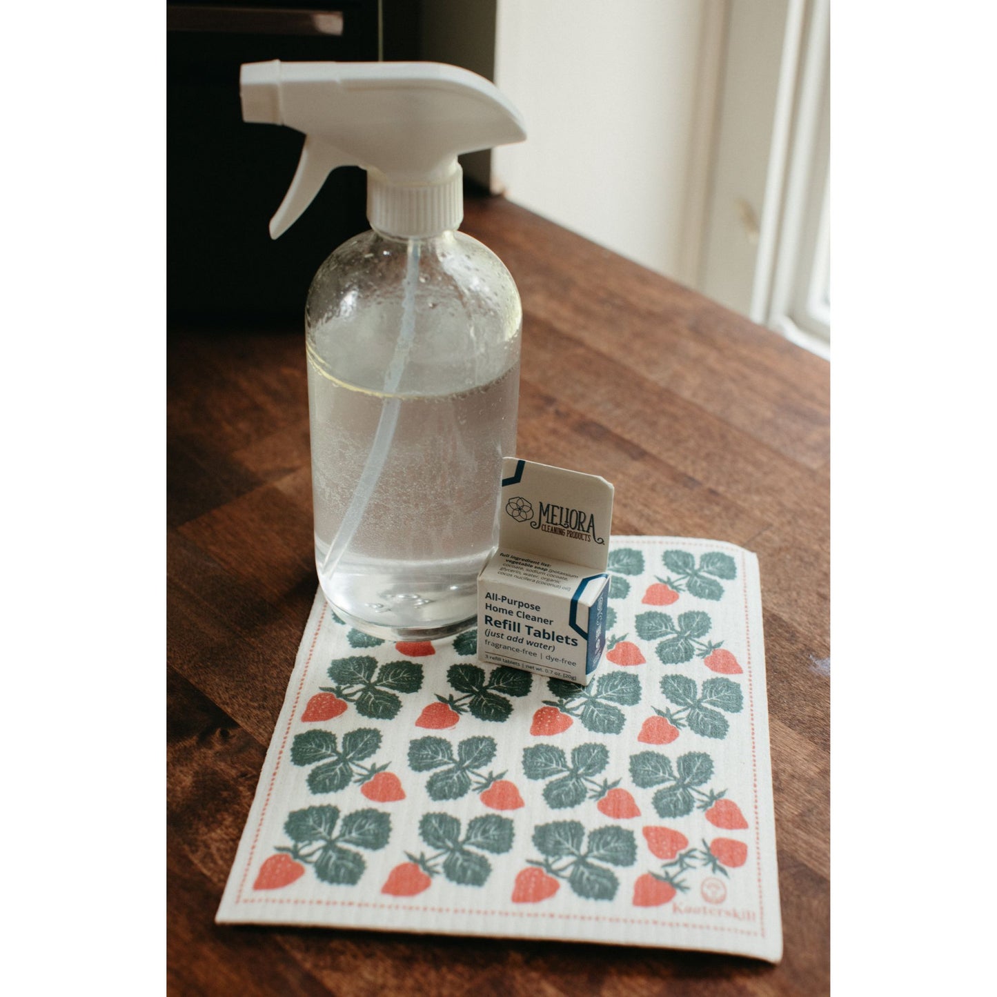 Strawberry dishcloth on a table with cleaning glass bottle and refill tablets 