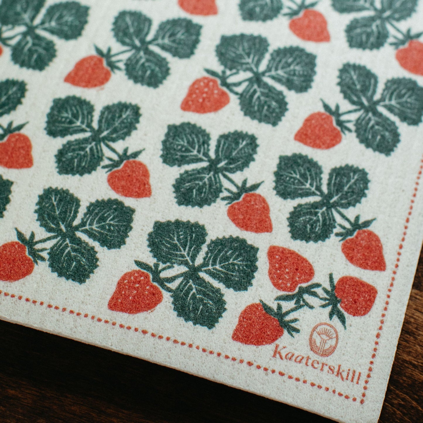 Swedish dishcloth with strawberrys and kaaterskill logo on a wooden table