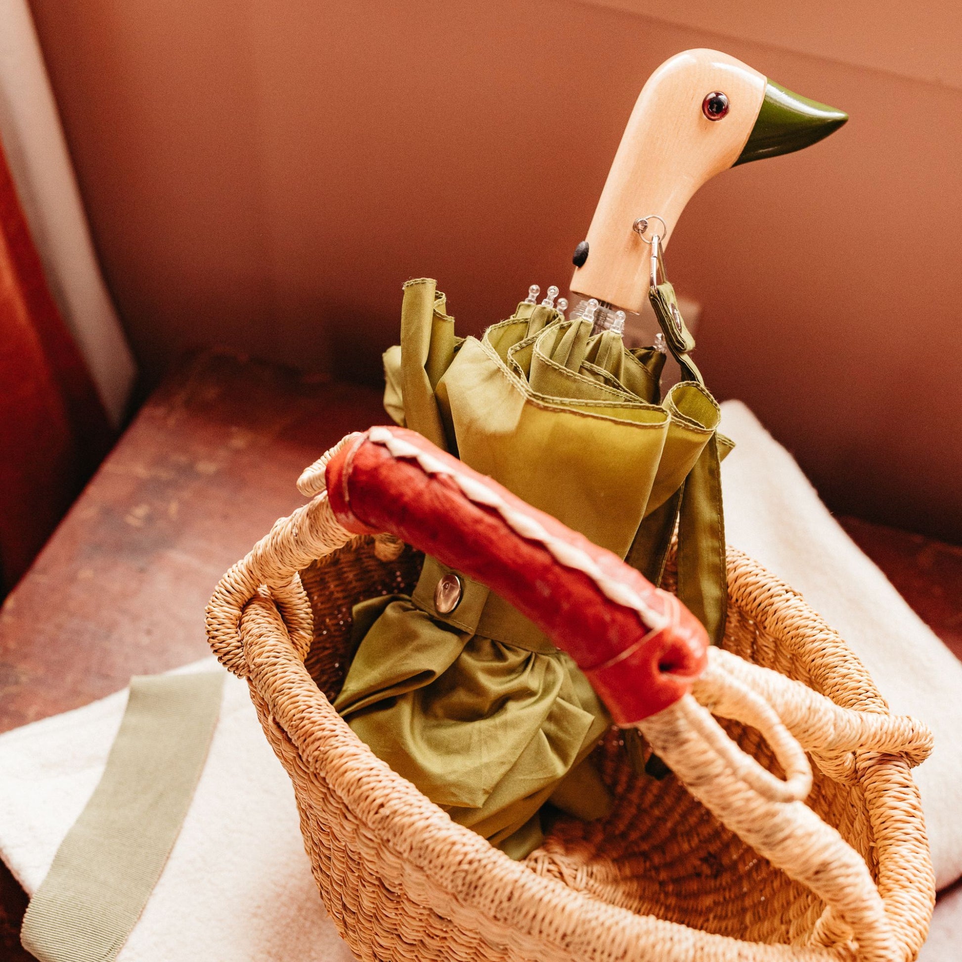 umbrella in olive with birchwood handle in the shape of duck head resting in a basket