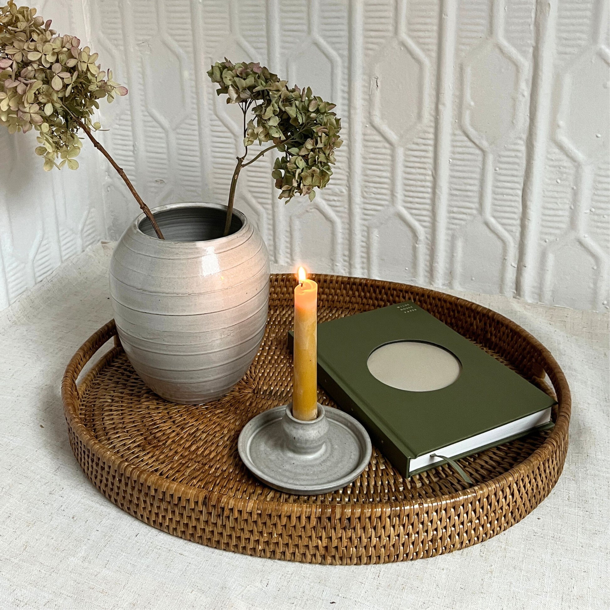 Decorative tray with a vase, candle, and book against a textured wall.