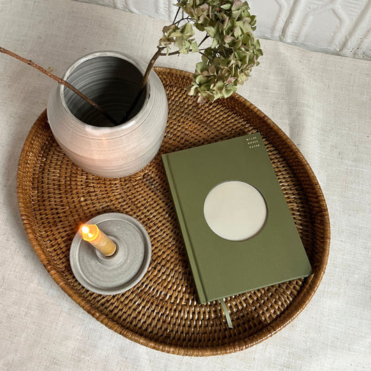 Green notebook, candle, and vase on a woven tray with a light background