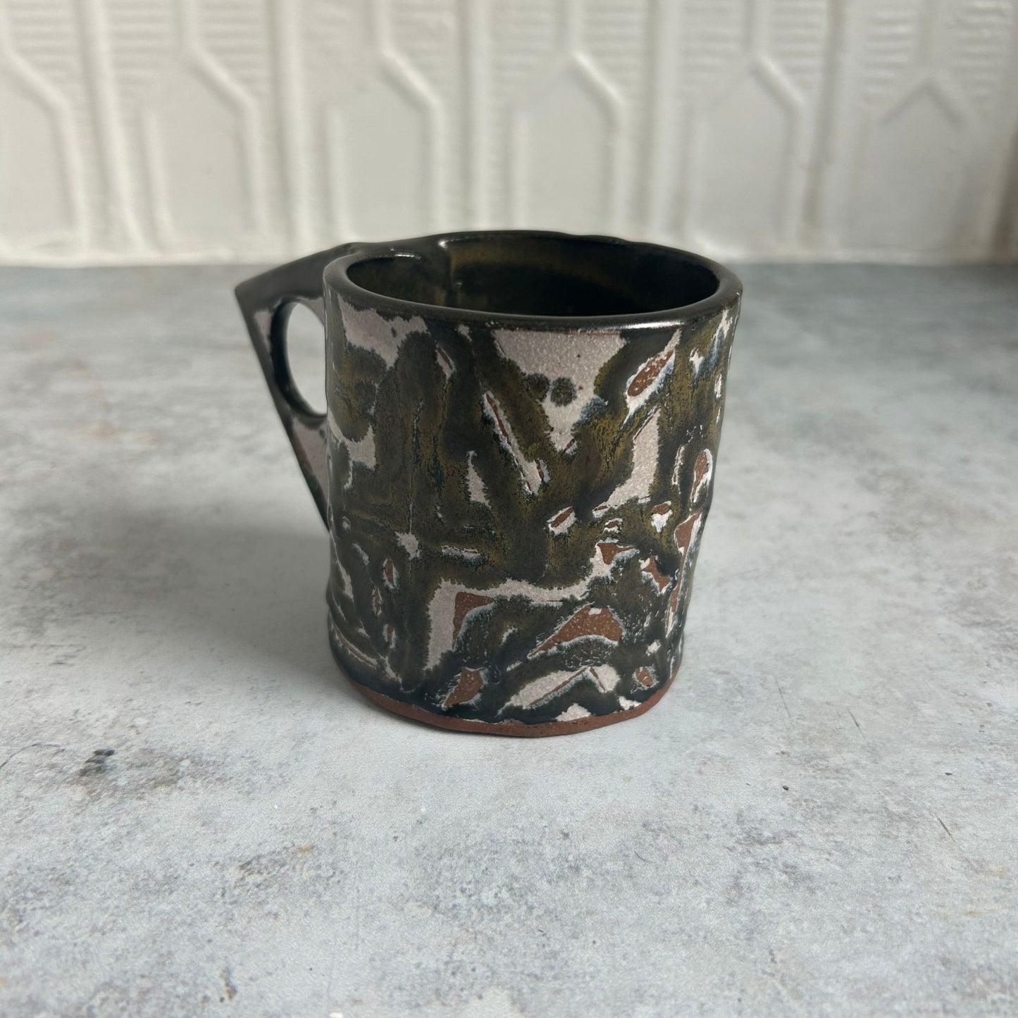Black, green, white, and red patterned mug with a triangle handle. 