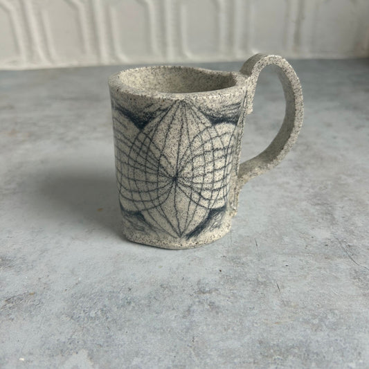 White speckled mug with a drawn lined pattern across it.