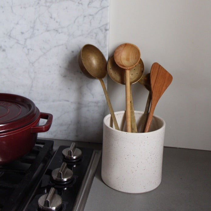 5 inch tall ceramic stoneware crock in white speckle glaze pictured with wood and metal cooking utensils next to stove