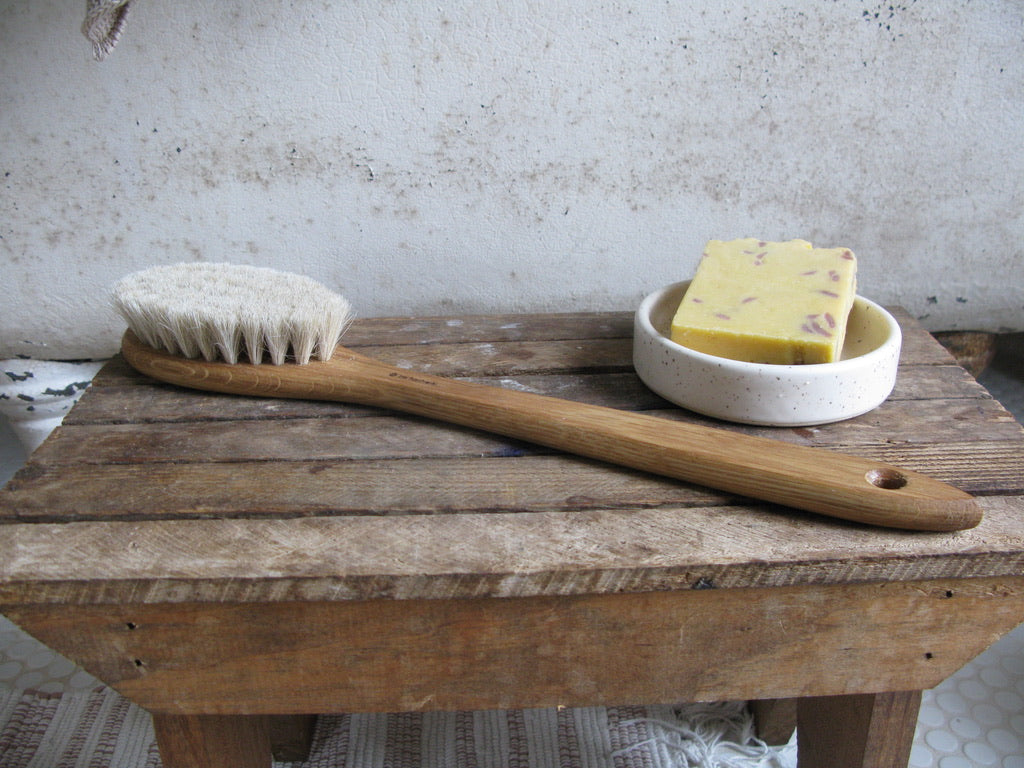 15.35 inch long oak bathing brush with horsehair bristles and hole for hangnig shown with soap in a ceramic dish