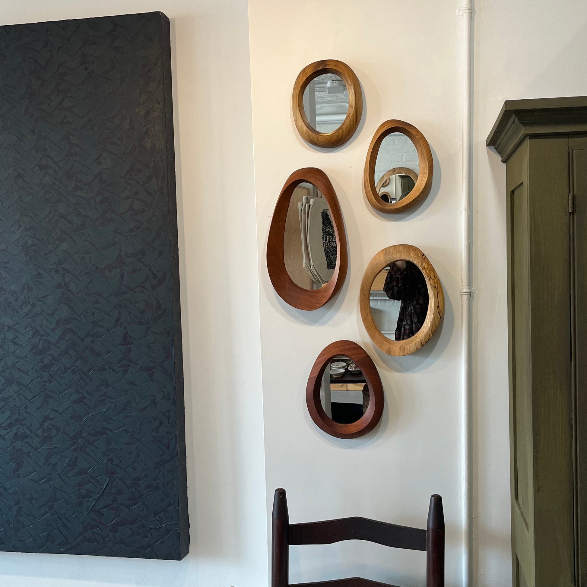various sizes of hand-carved wooden wall mirrors each with one-of-a-kind organic shape and curves shown in butternut cherry and walnut