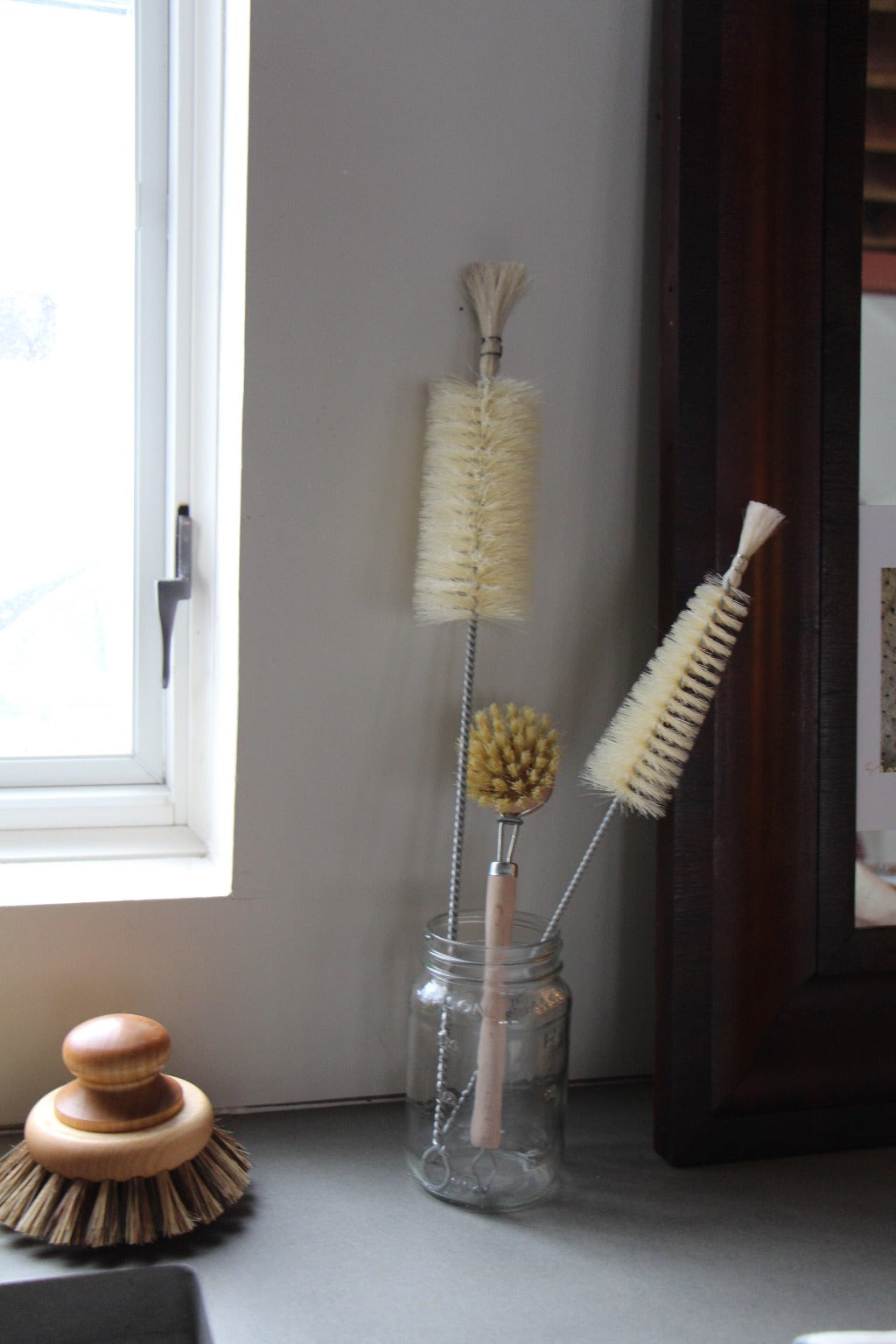 Narrow and long bottle cleaning brushes shown in jar on countertop with handled dish brush
