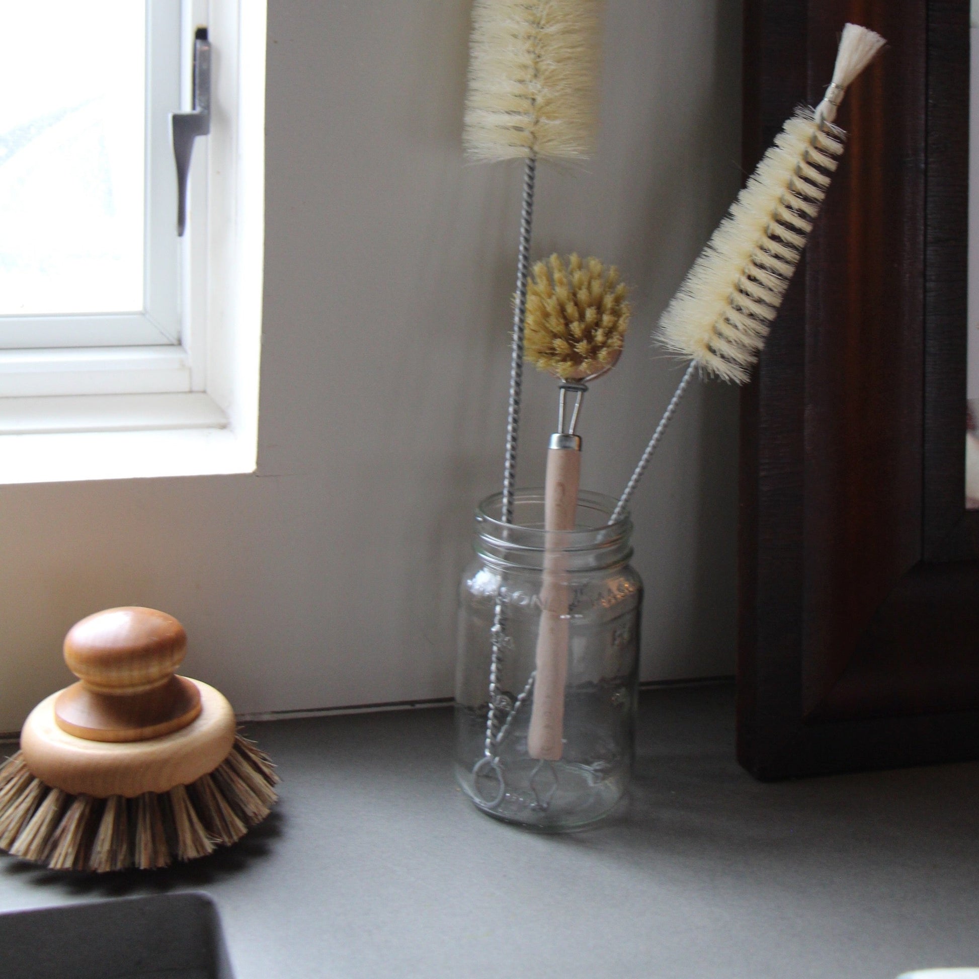 Sturdy brush for pots and pans with round maple handle and natural bristles, shown with several dish and glass brushes
