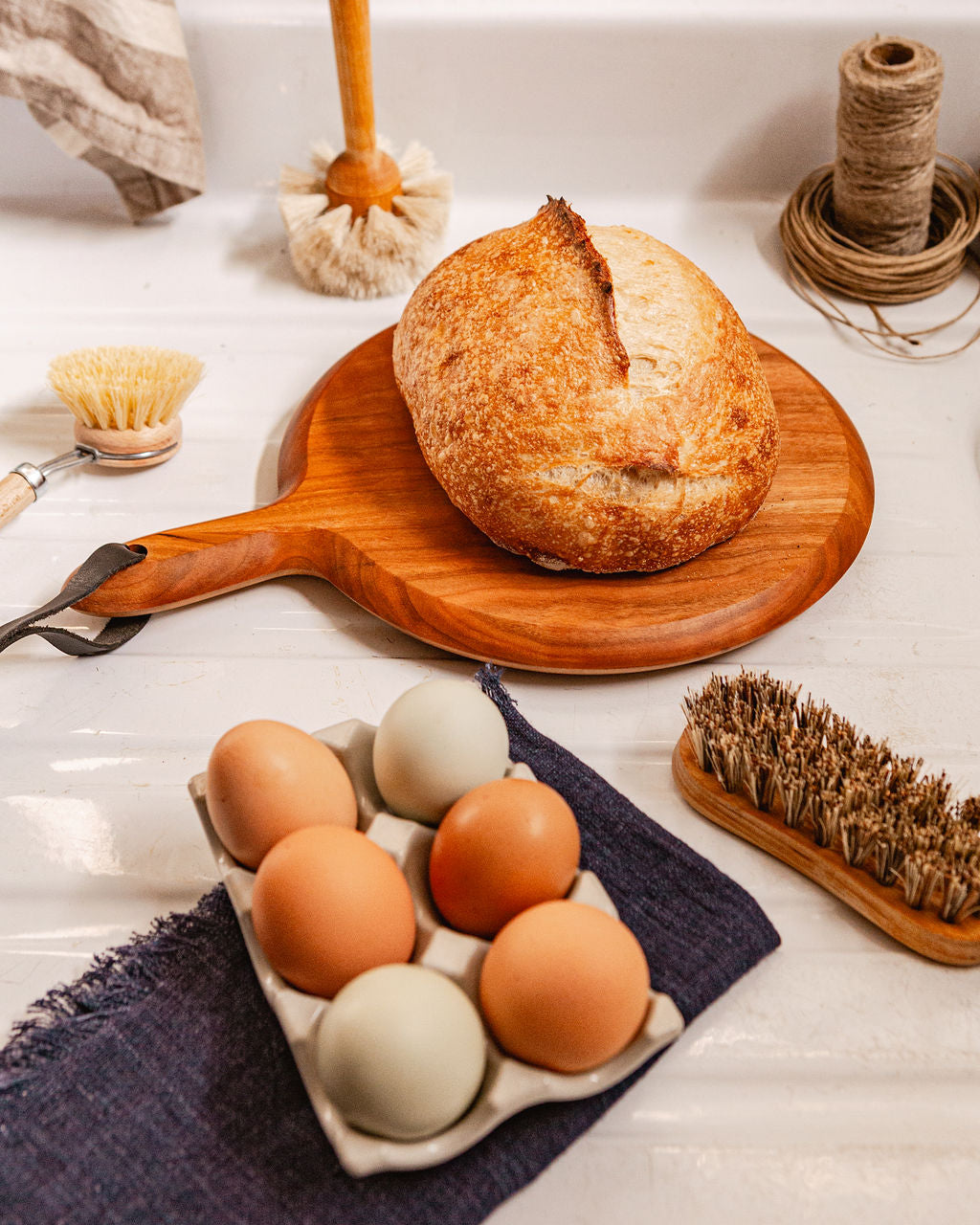 Medium circular cutting board in cherry with handle and leather strap shown with loaf of bread