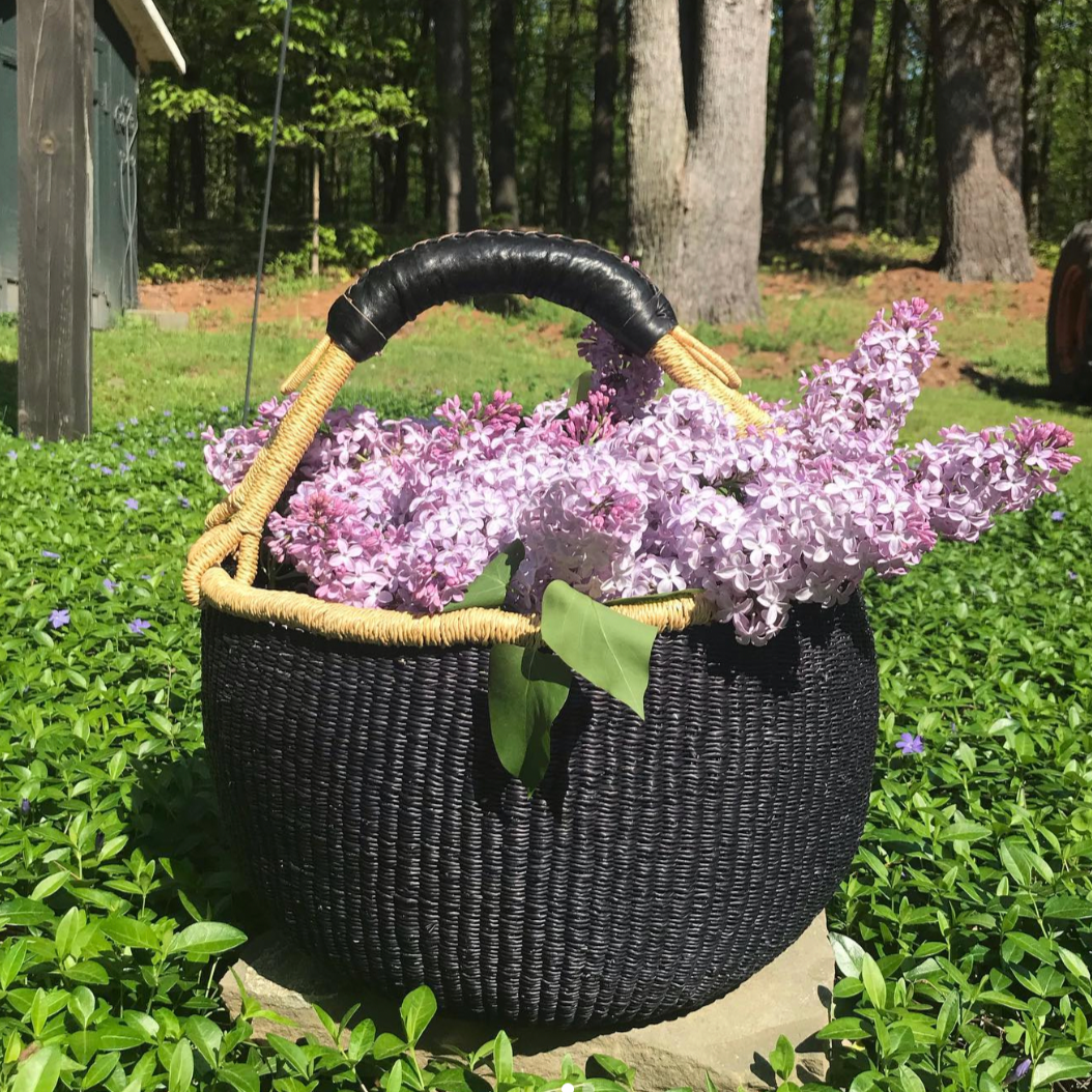 Handwoven black Bolga basket shown outdoors with fresh flowers inside