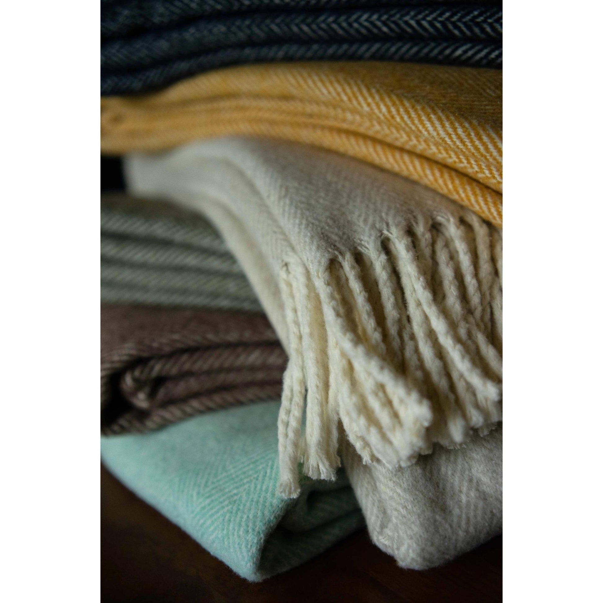 Close-up of stack of folded brushed cotton throw blankets with herringbone pattern in various colors