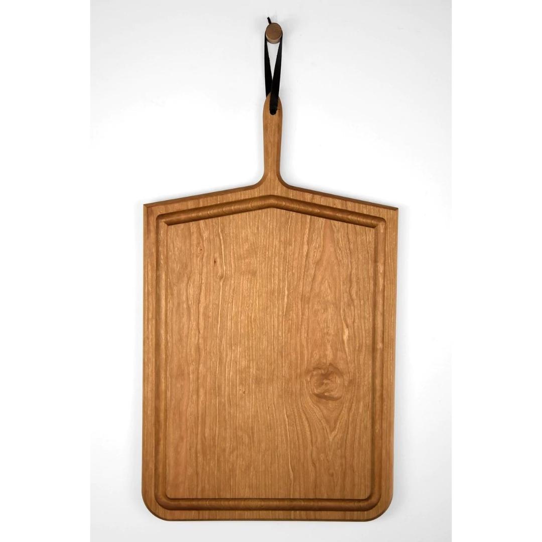 Oversized rectangular carving board in cherry wood with handle and leather strap hanging on wall hook