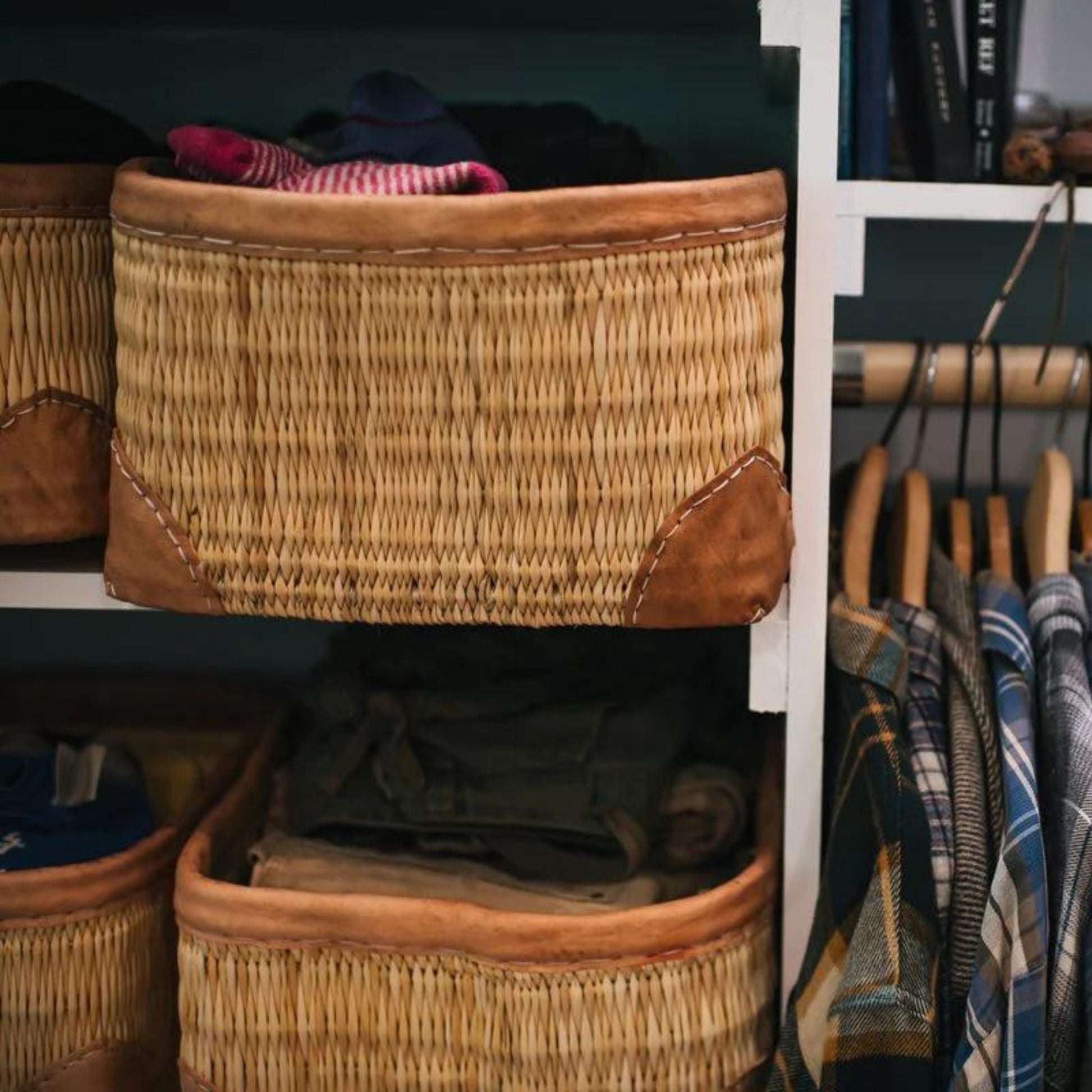 Woven palm and leather-trimmed rectangular baskets shown in use as closet storage