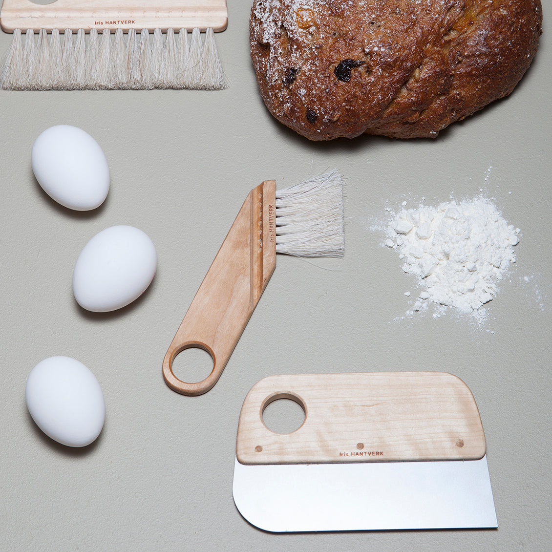 dough scraper with oil-treated birch handle and a strong stainless steel blade shown with eggs, bread and pastry brushes