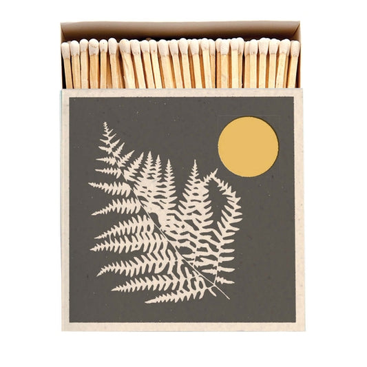 Square box of long wooden matches with image of white fern on black background with golden sun