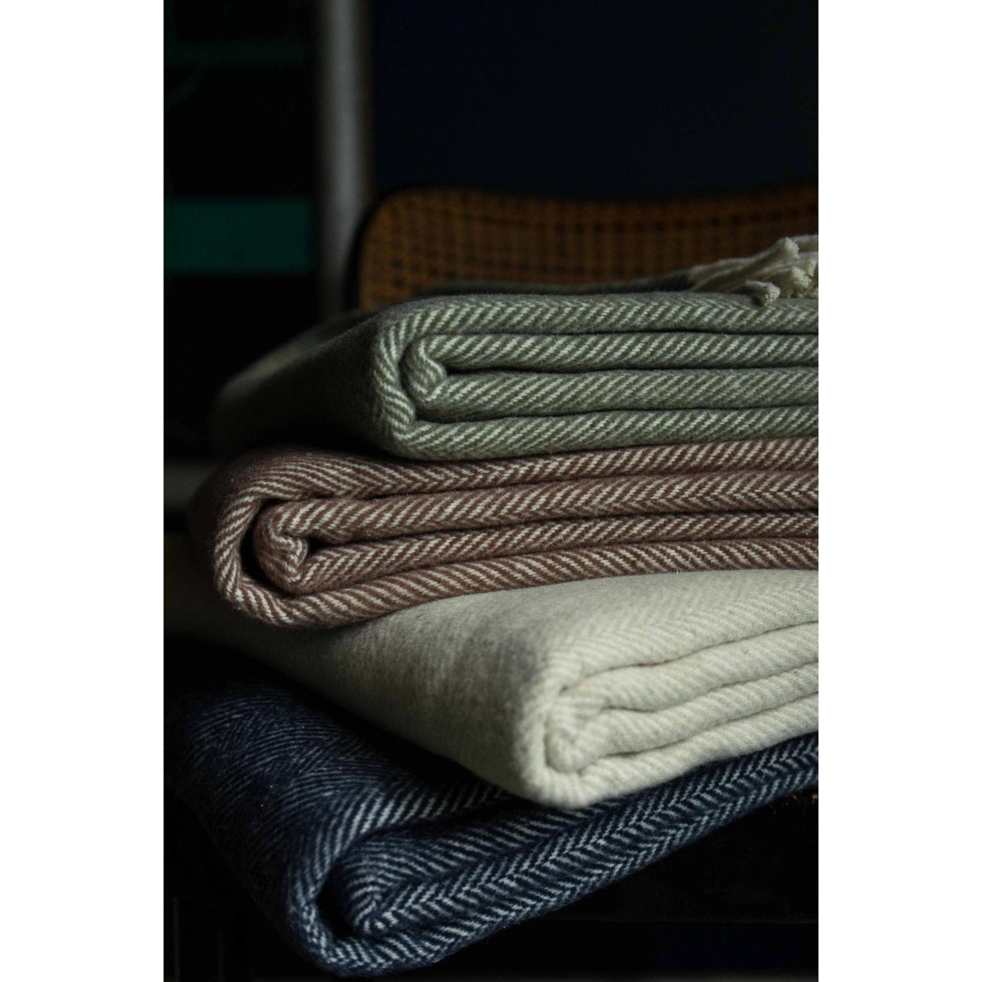 Close-up of stack of folded brushed cotton throw blankets with herringbone pattern in various colors