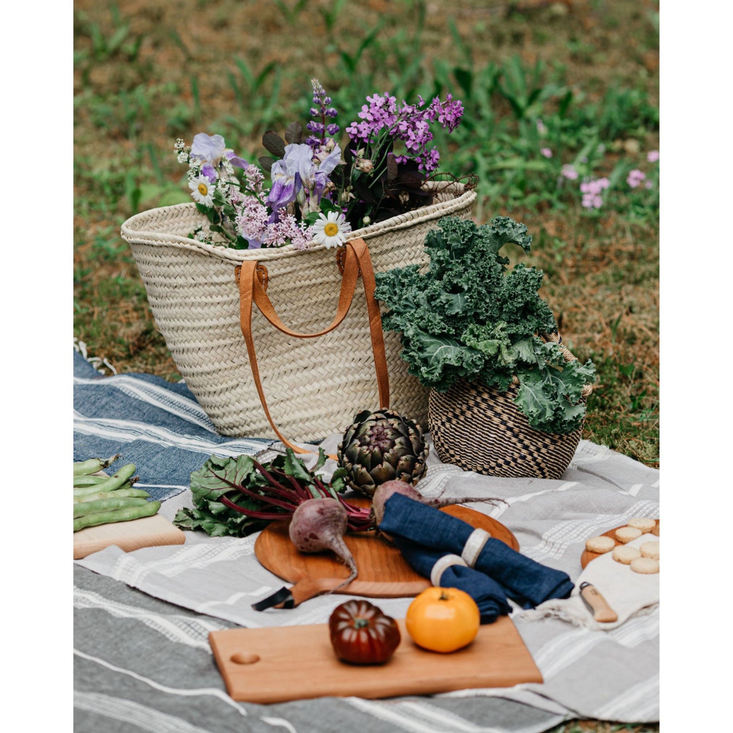 French Market Tote Basket with flowers in it sitting on a picnic blanket with some different foods