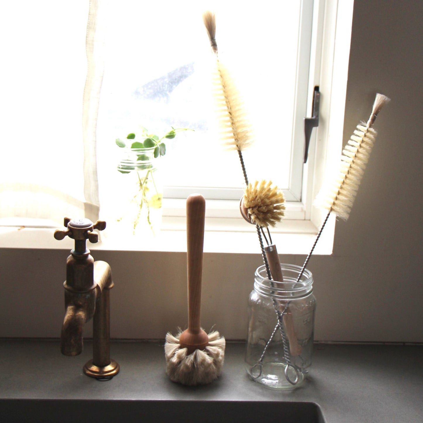 Glas brush sitting on a sink next to a glass full of other cleaning brushes.