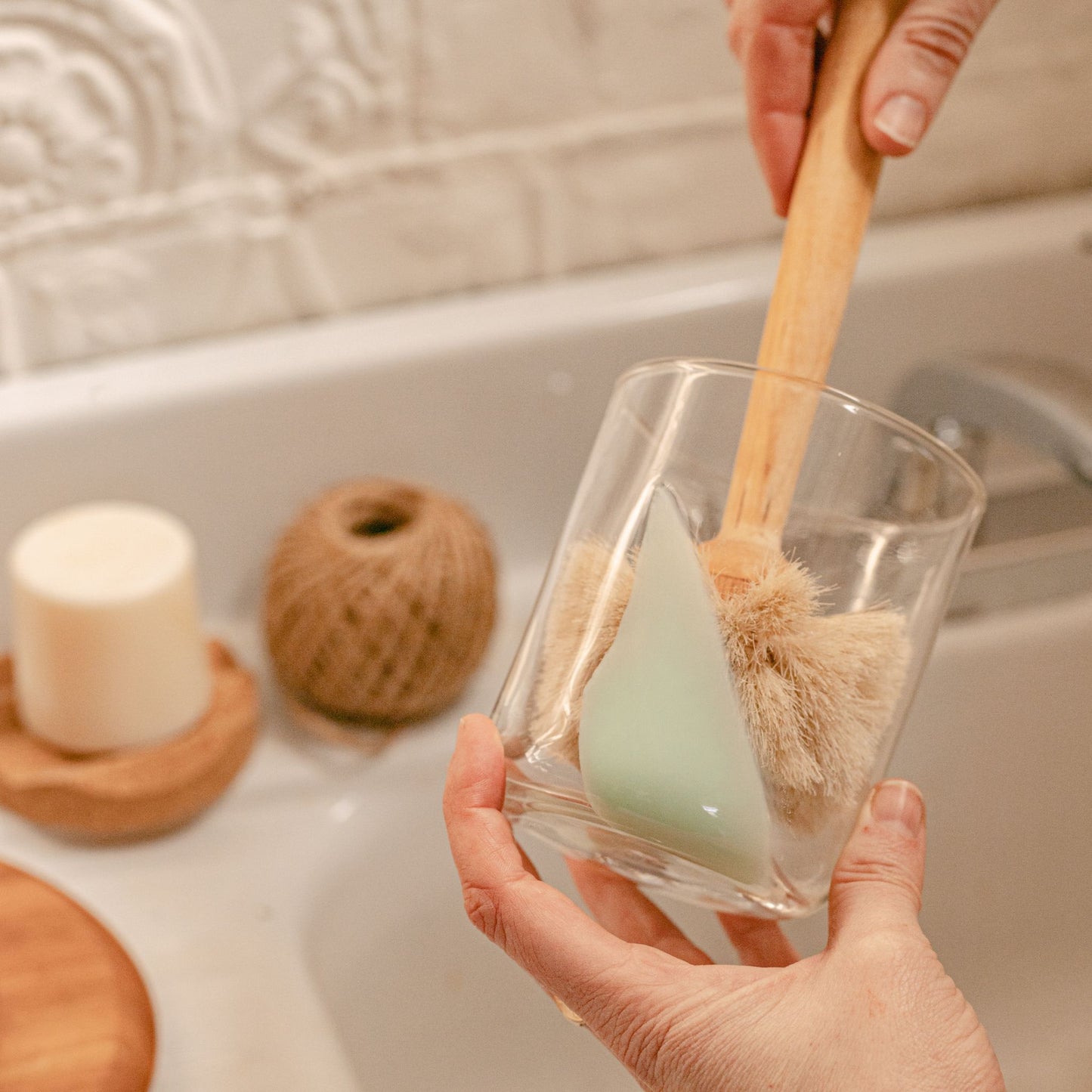 Glass brush cleaning a glass. Sink with soap in the background