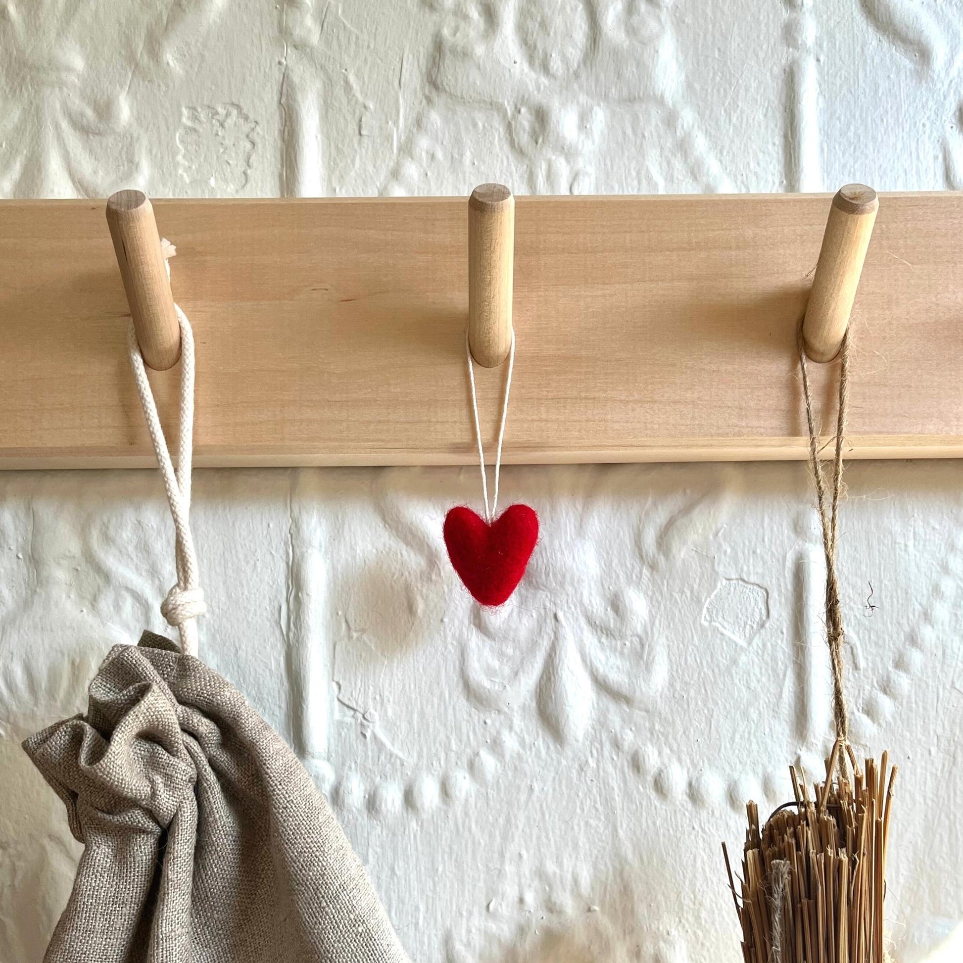 Handmade felted wool red hearts hanging on wall rail of hooks