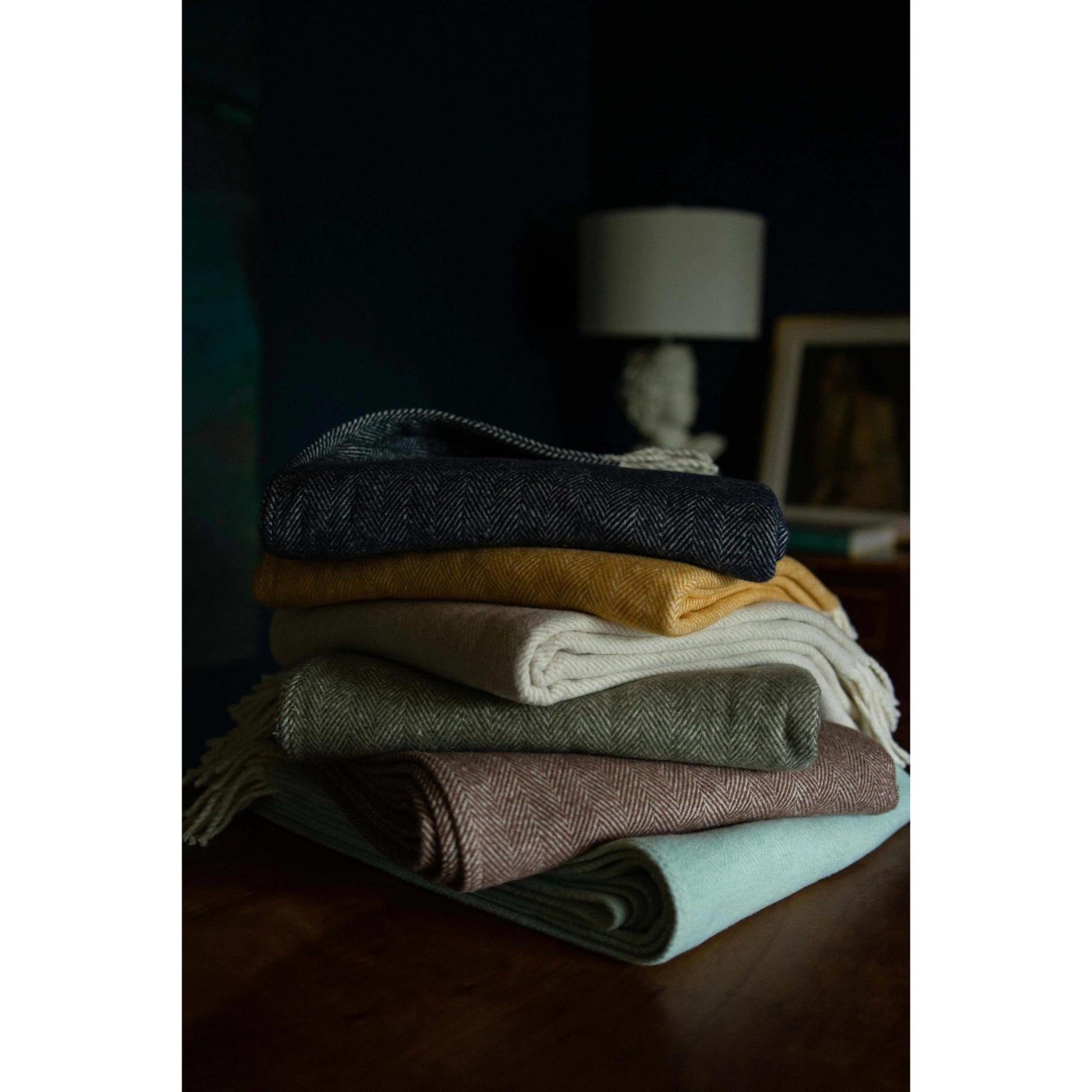 Stack of folded brushed cotton throw blankets with herringbone pattern in various colors